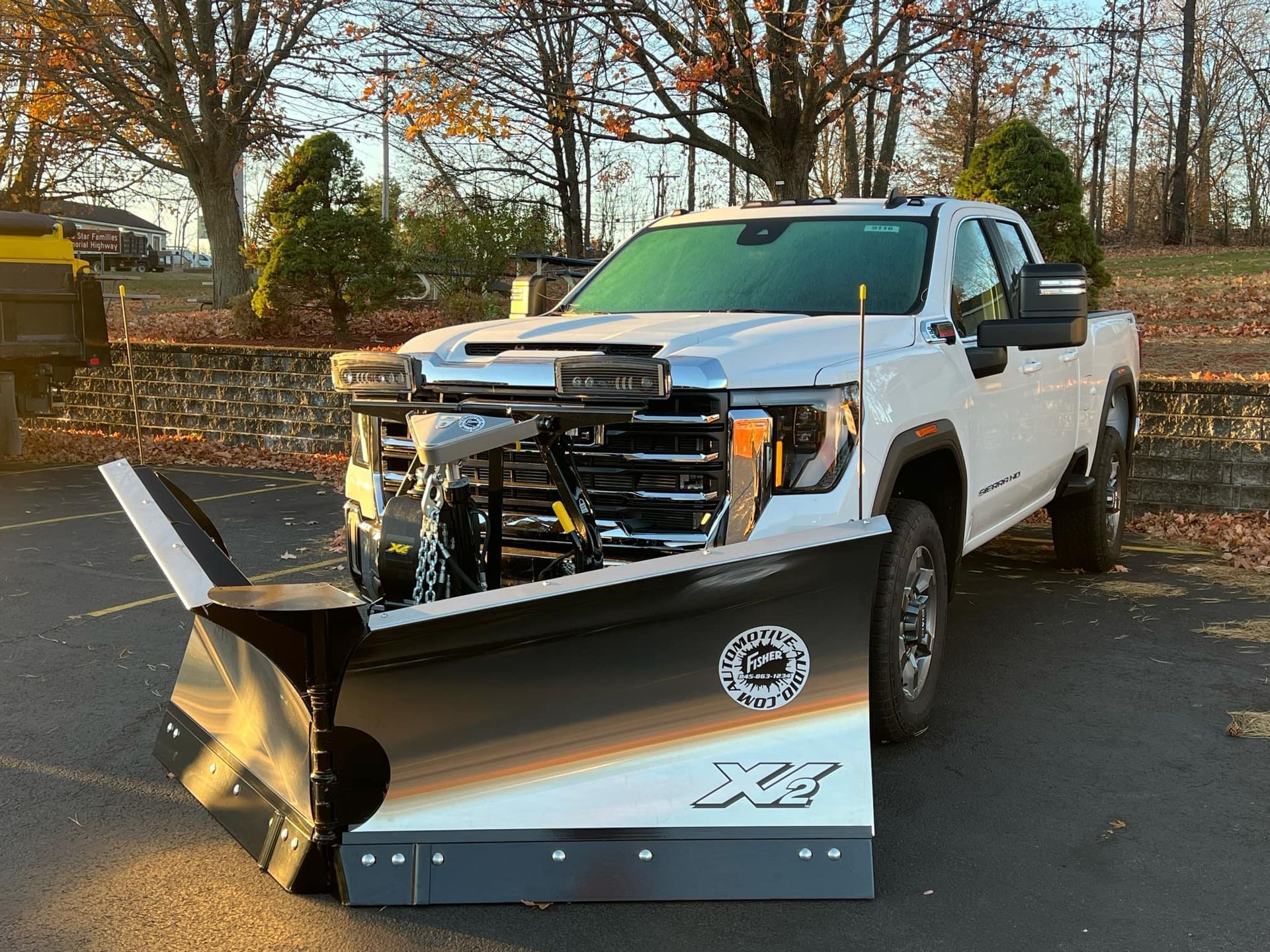 A white truck with a snow plow attached to it is parked in a parking lot.