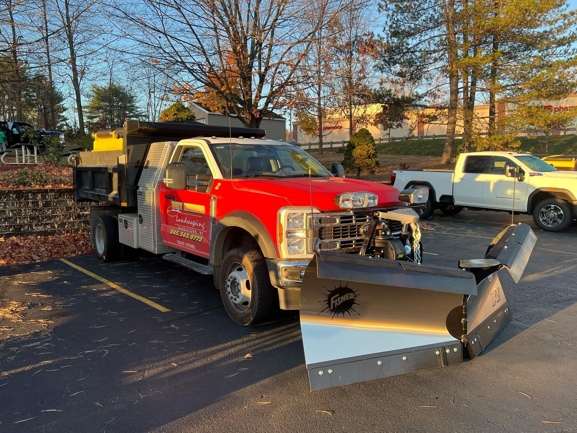 A red truck with a snow plow on the front is parked in a parking lot.