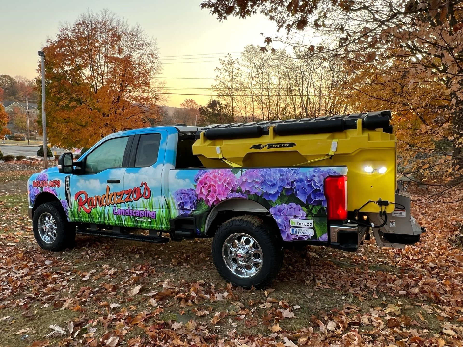 A truck with flowers painted on it is parked in a pile of leaves.
