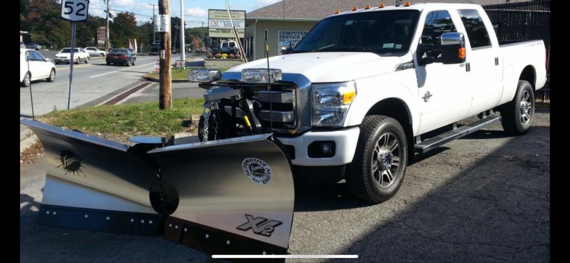 A white truck with a snow plow attached to it is parked on the side of the road.