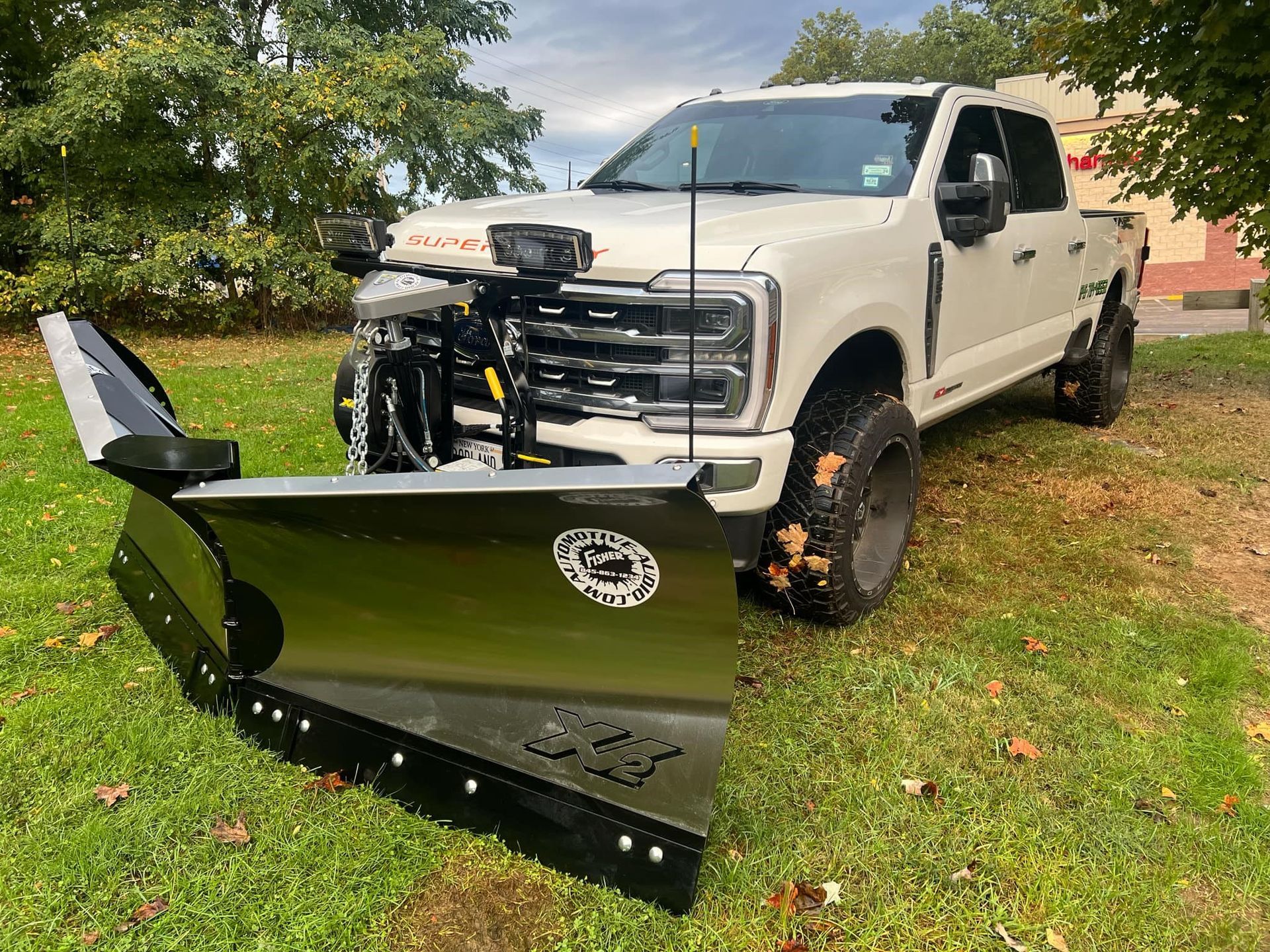 A white truck with a snow plow on the front is parked in the grass.