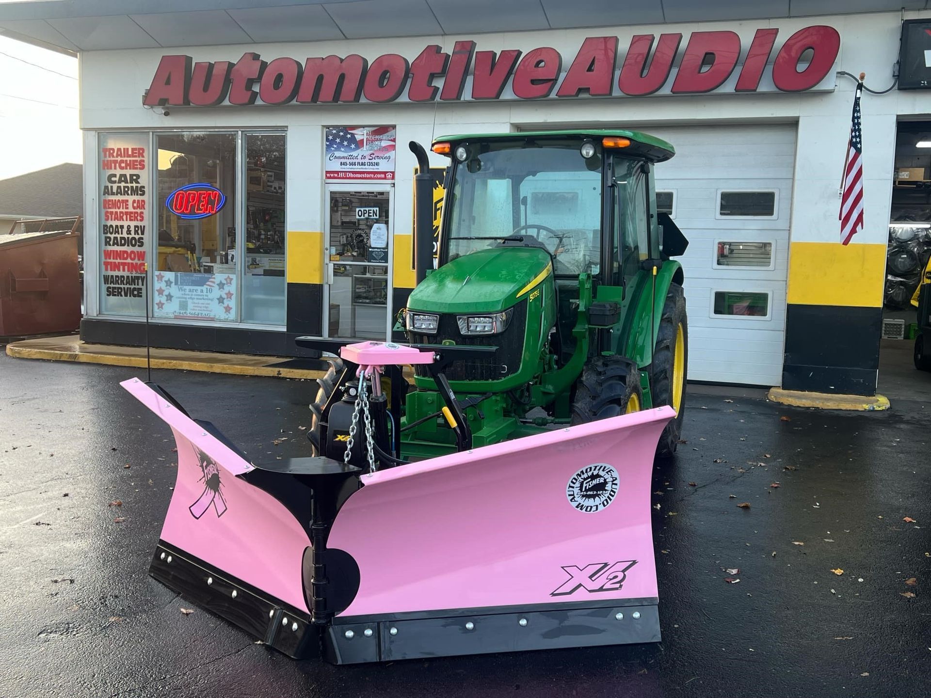 A green tractor with a pink plow is parked in front of a store