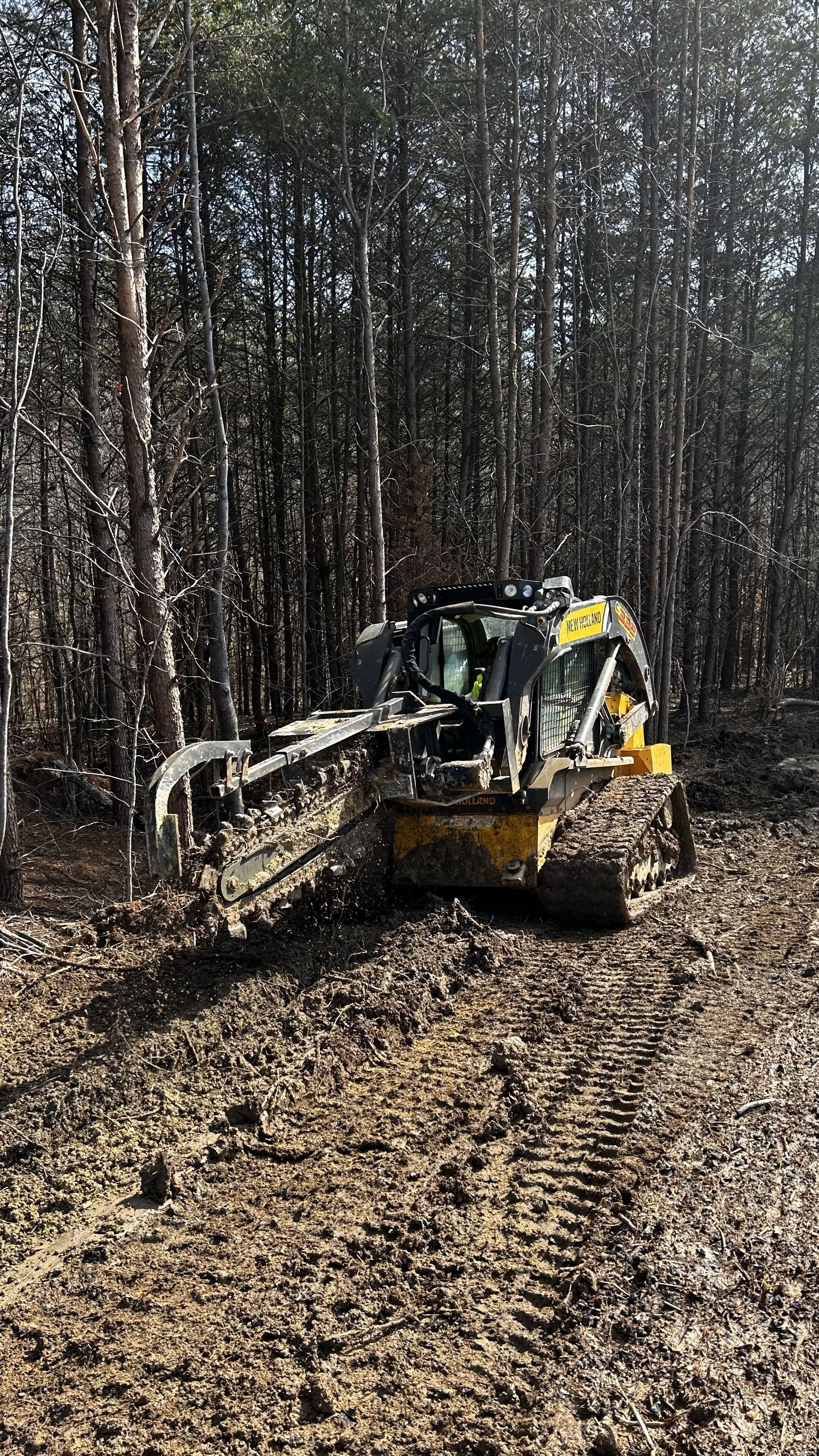 A bulldozer is driving through a muddy field in the woods.