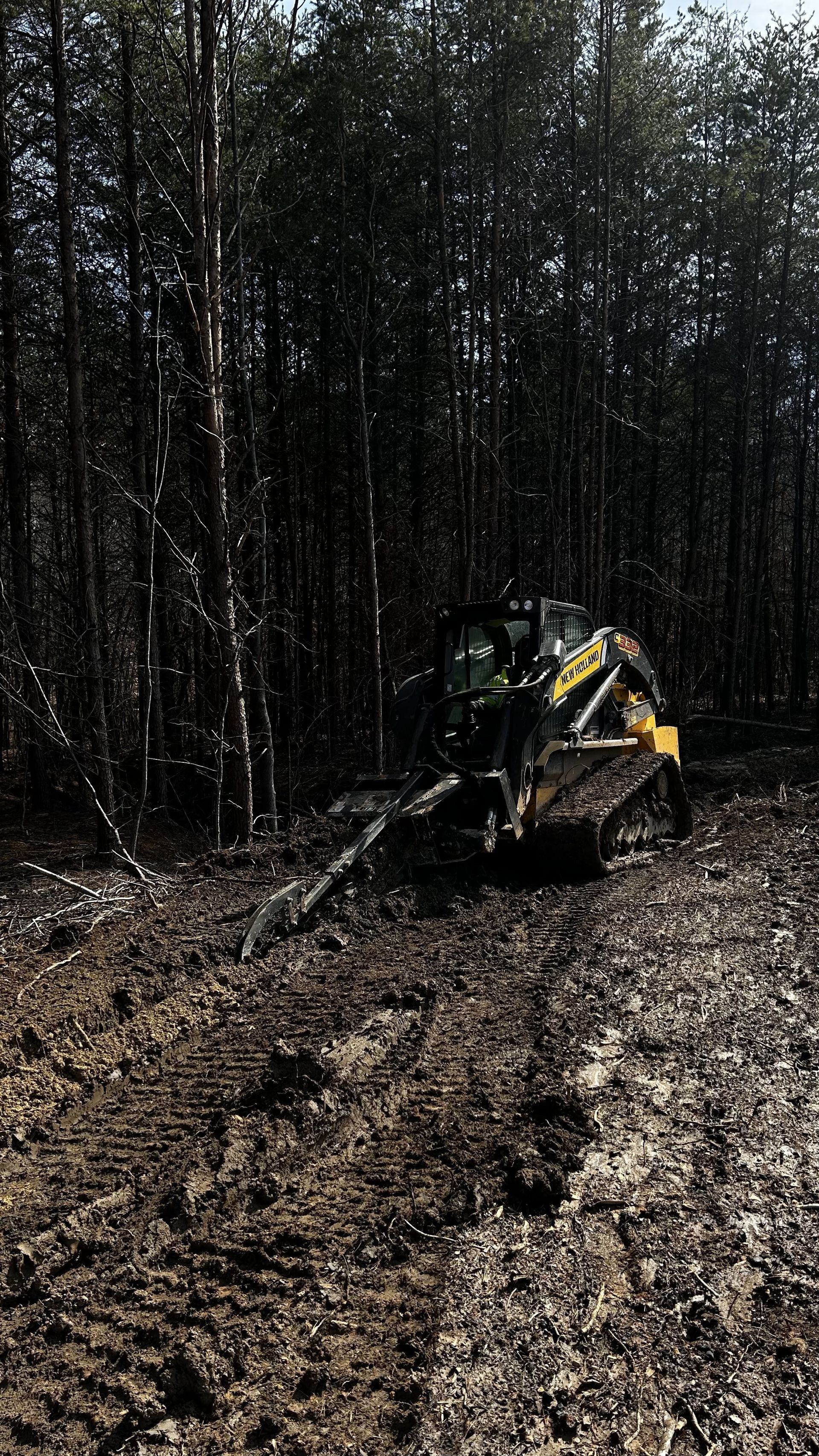 A bulldozer is driving through a muddy field in the woods.