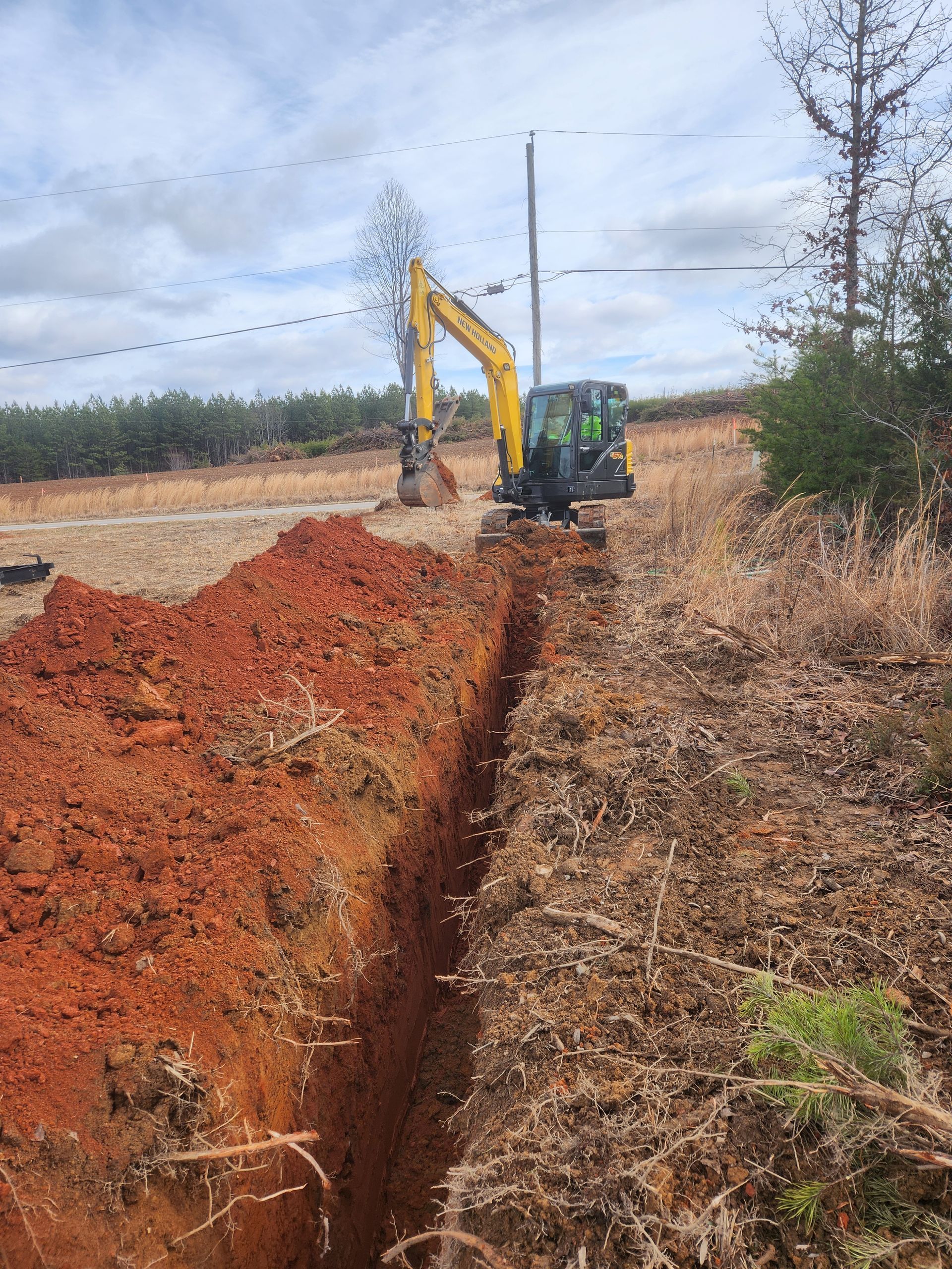 A yellow excavator is digging a trench in a field.