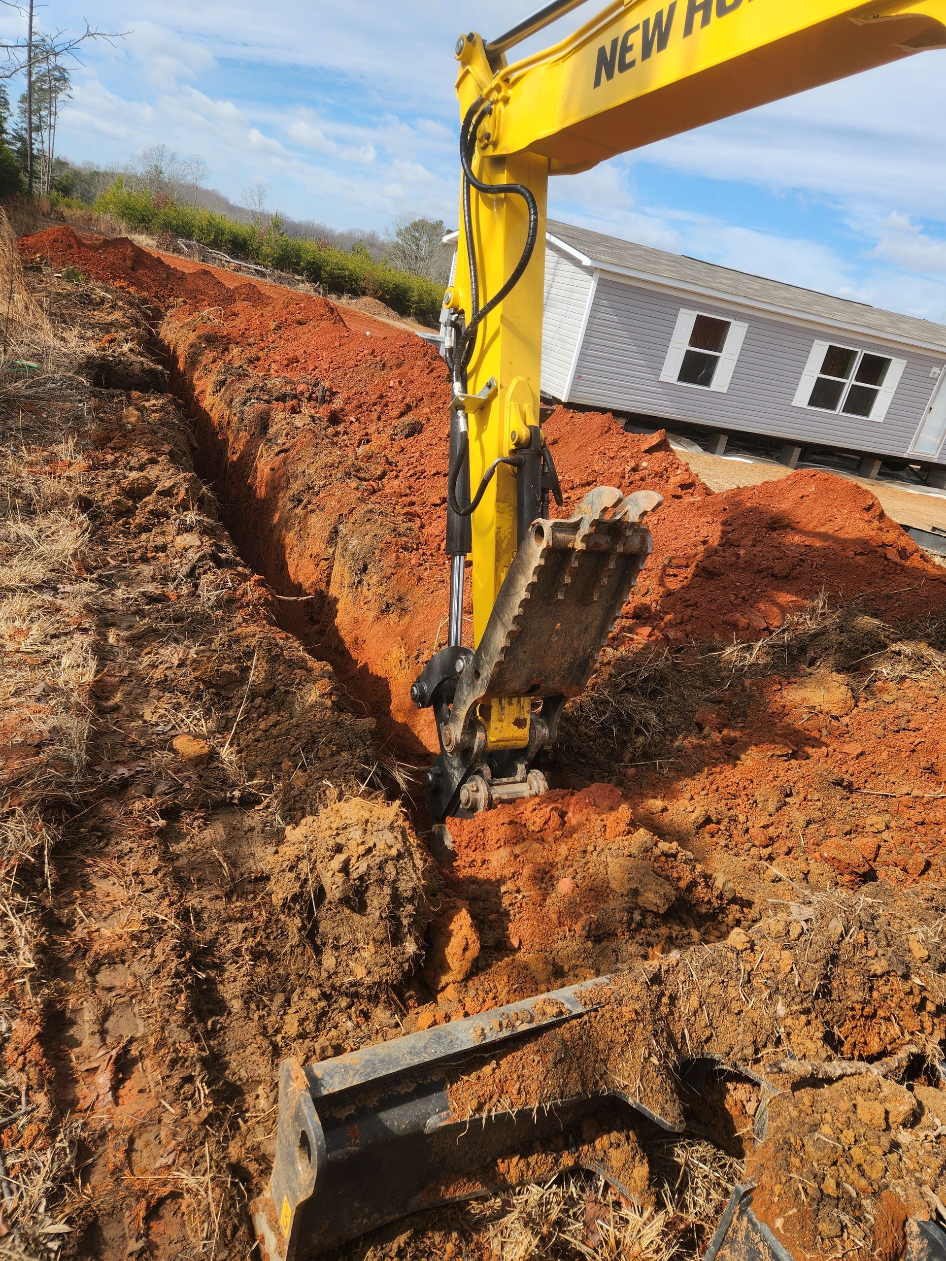 A yellow excavator is digging a trench in the dirt.