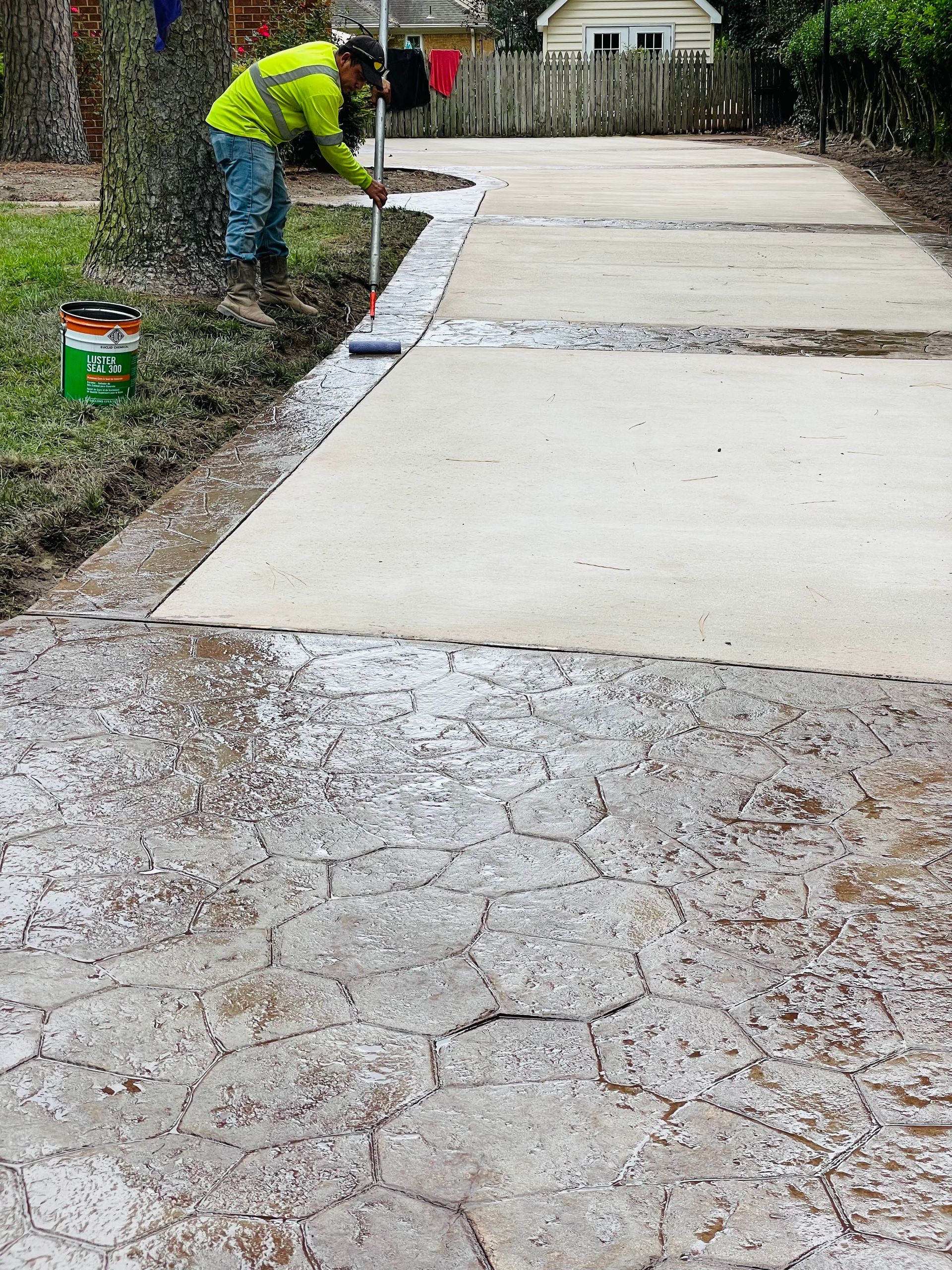 Worker pouring concrete on a driveway beside a house, smoothing a fresh section.