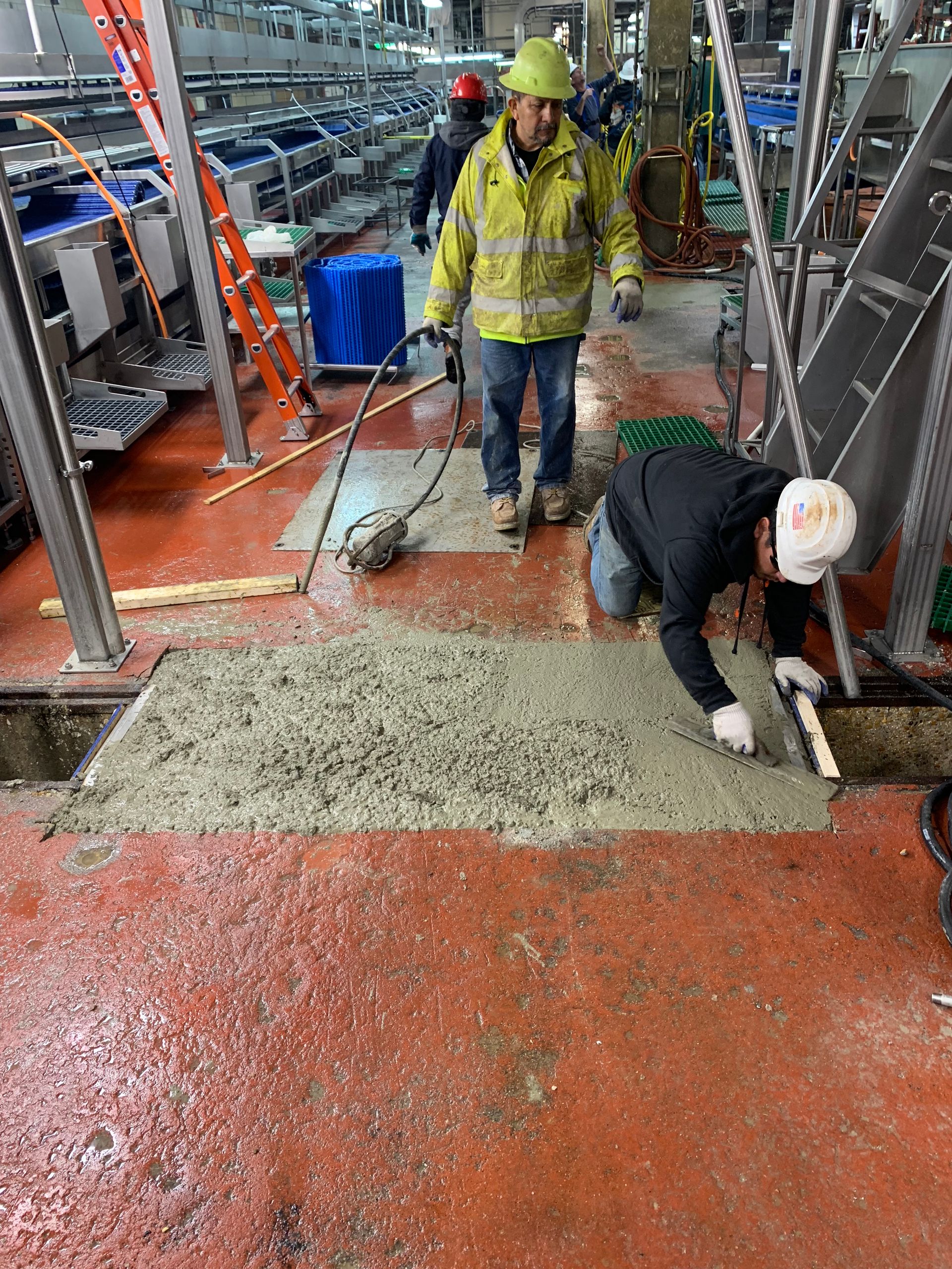 Construction workers pouring concrete on a red floor in an industrial setting