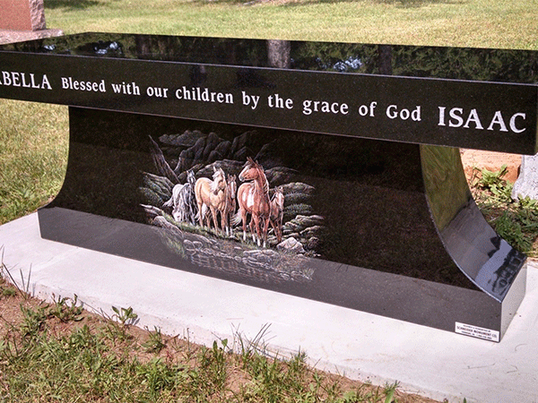 Black granite bench with names and text, a painted scene of horses, outdoors.