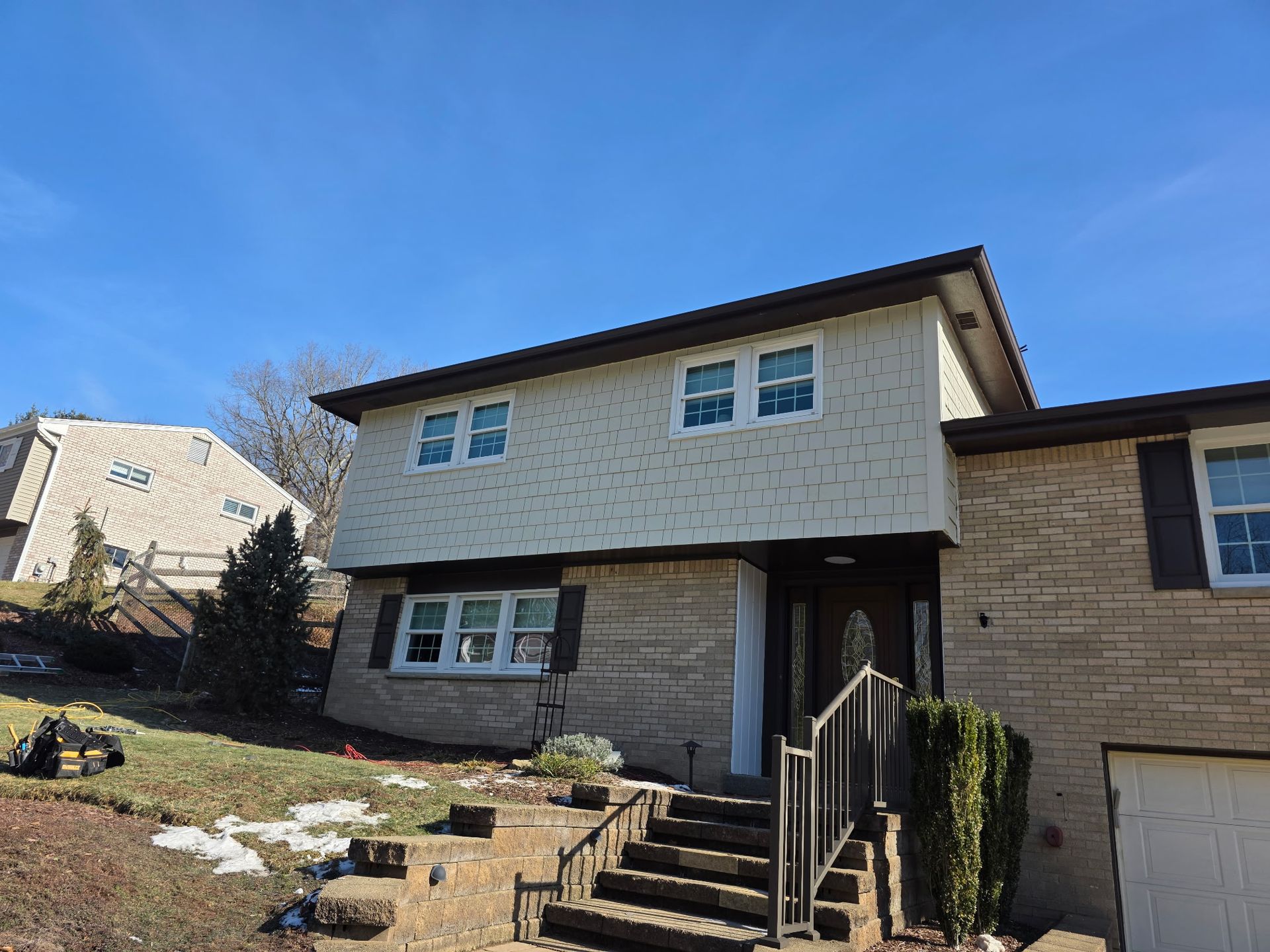 A two-story split-level home with beige stone and light-colored siding, featuring a front staircase and an attached garage.