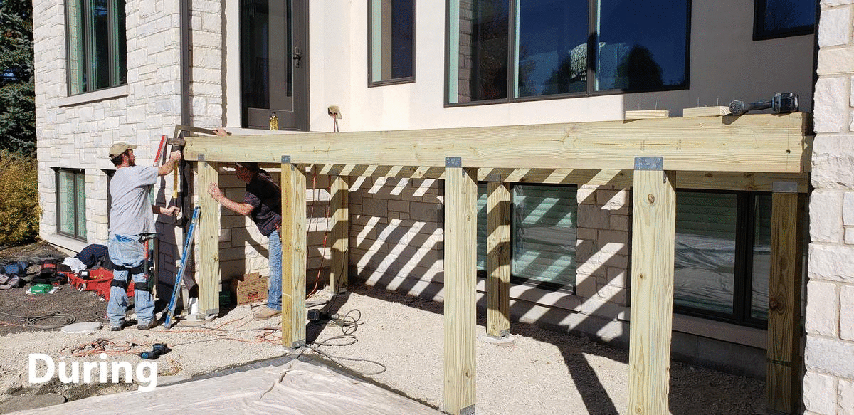 Construction of a wooden pergola outside a building. Workers assemble the structure near windows.
