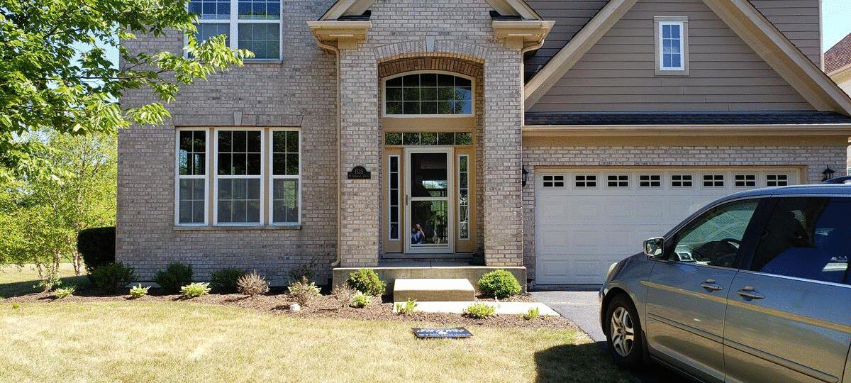 A two-story brick house with a garage and a car in front on a sunny day.