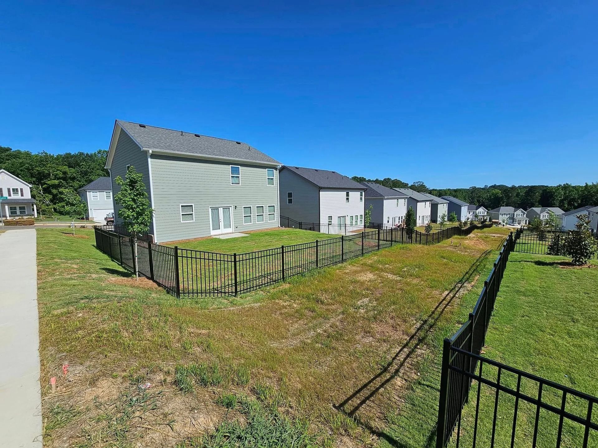 Row of pale houses behind black fences beside a grassy field under a bright blue sky