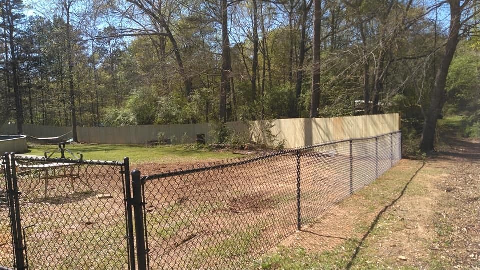 Chain-link fenced dog park with dirt ground, benches, and trees in a sunny wooded area
