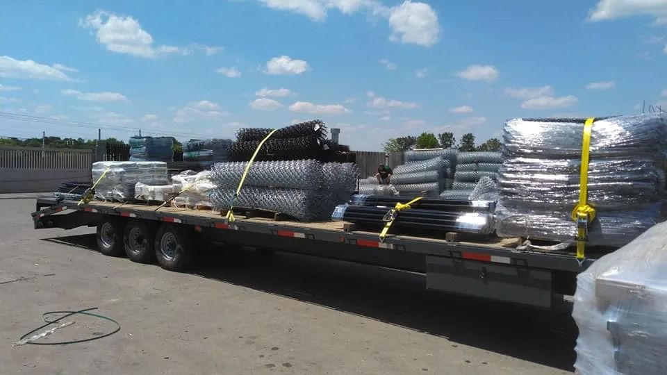 Flatbed truck loaded with coiled metal pipes and wrapped materials in a sunny industrial lot