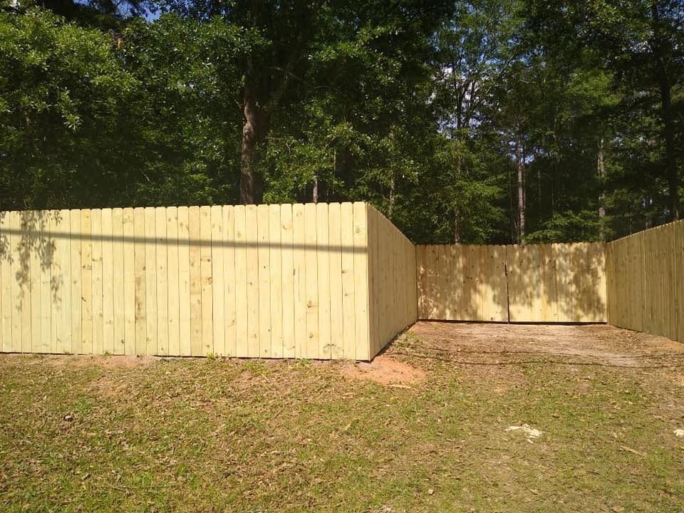 Wooden fenced enclosure in a grassy, wooded yard with trees overhead
