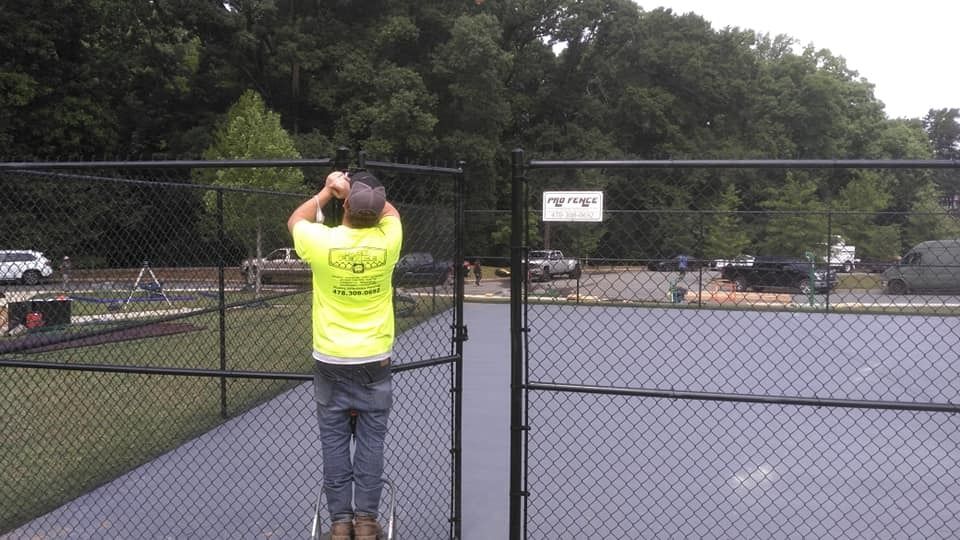Person in neon yellow shirt standing by a chain-link gate at an empty tennis court