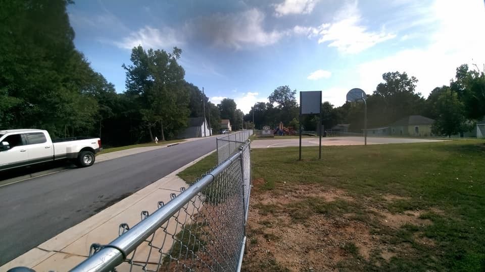 Chain-link fence beside a road with a white pickup truck and trees under a cloudy blue sky