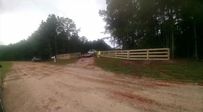 Dirt road curving past a white fence and trees, with a parked car in the distance