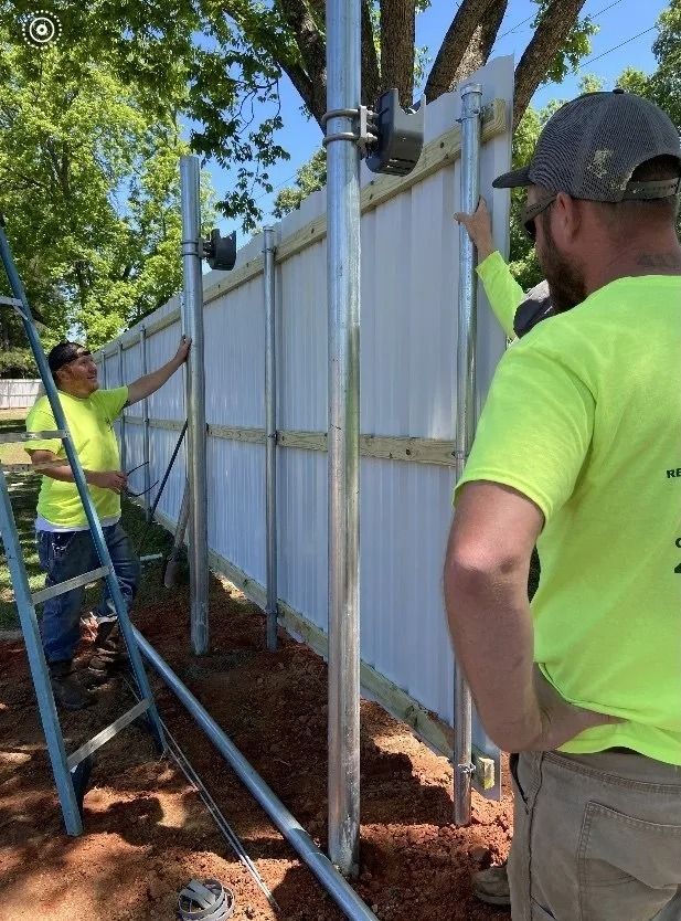 Workers installing a white fence outdoors in a sunny yard with shovels and posts