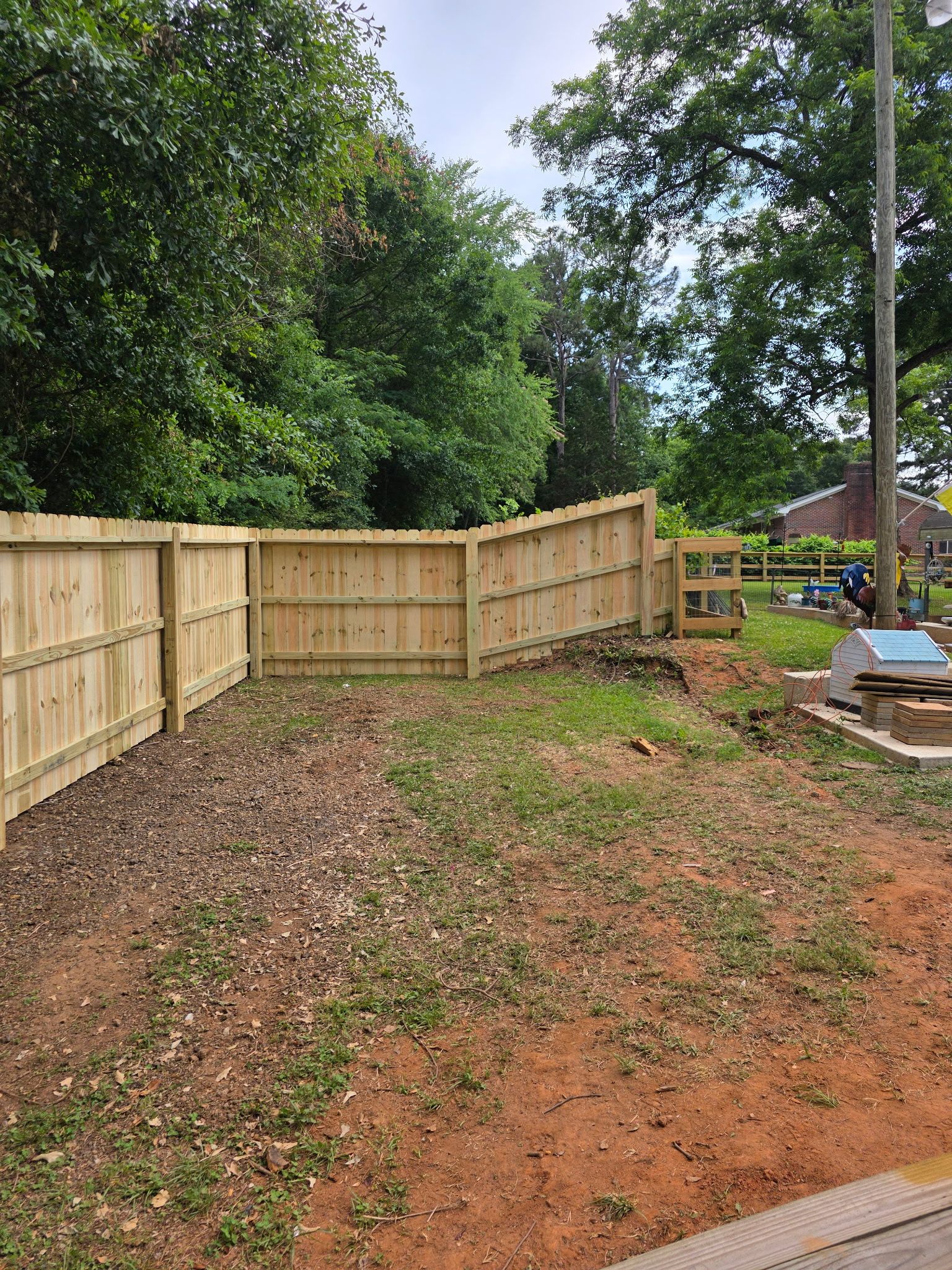 New wooden fence corner beside a leaf-covered yard and trees under a cloudy sky