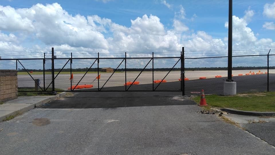 Closed black gate blocking a paved road by the waterfront under a cloudy sky