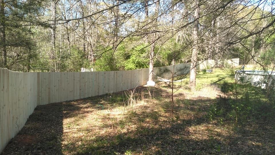 Wooded backyard with a white wooden fence and a small dirt path in sunlight