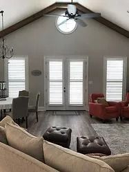 Living room with vaulted ceiling, fan, round window, white shutters, beige sofa, and red armchairs