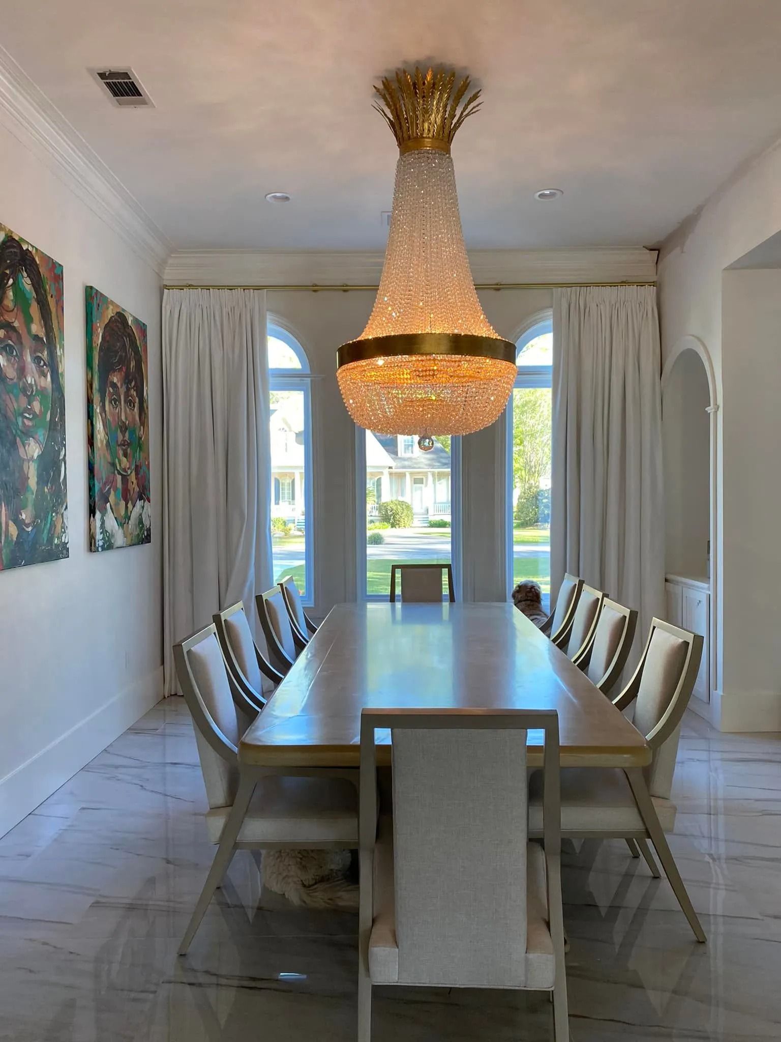 Elegant dining room with long table, upholstered chairs, chandelier, and tall windows overlooking greenery