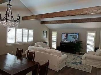 Living room with white sofas, wood beams, chandelier, and a TV on a console