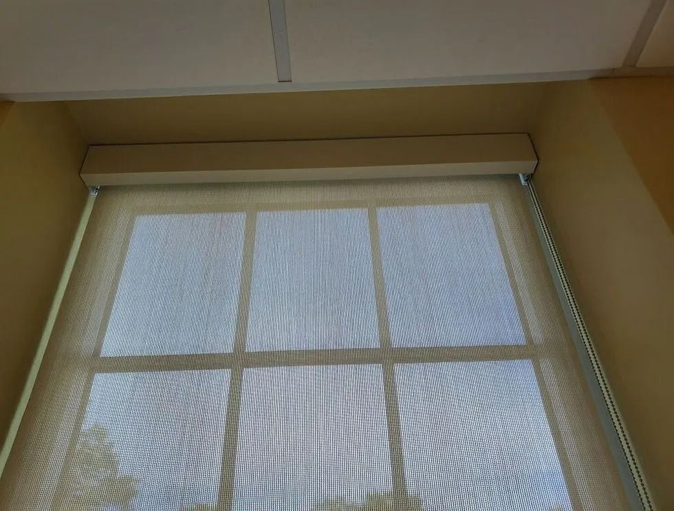 Window with white blinds and sheer curtains beneath a beige ceiling corner