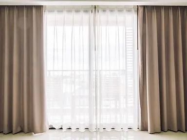 Sheer white and beige curtains framing a bright window in a minimalist room