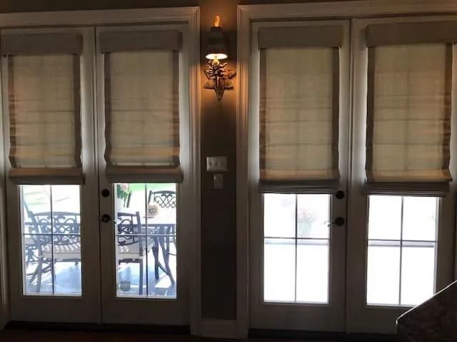 Interior view of French doors with beige blinds, opening to a patio and bright outdoor light