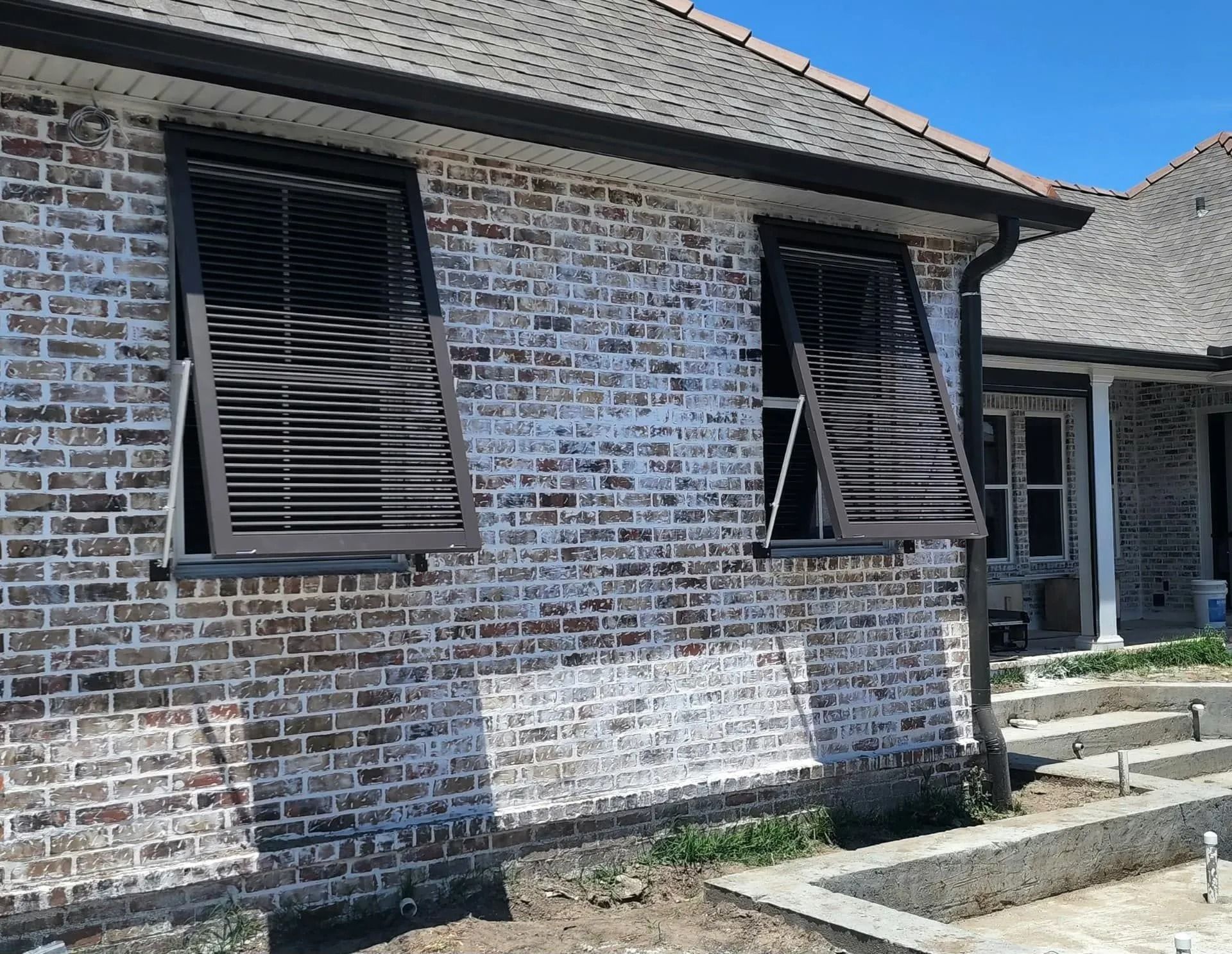 Brick house exterior with closed black shutters and a small concrete stoop in front.