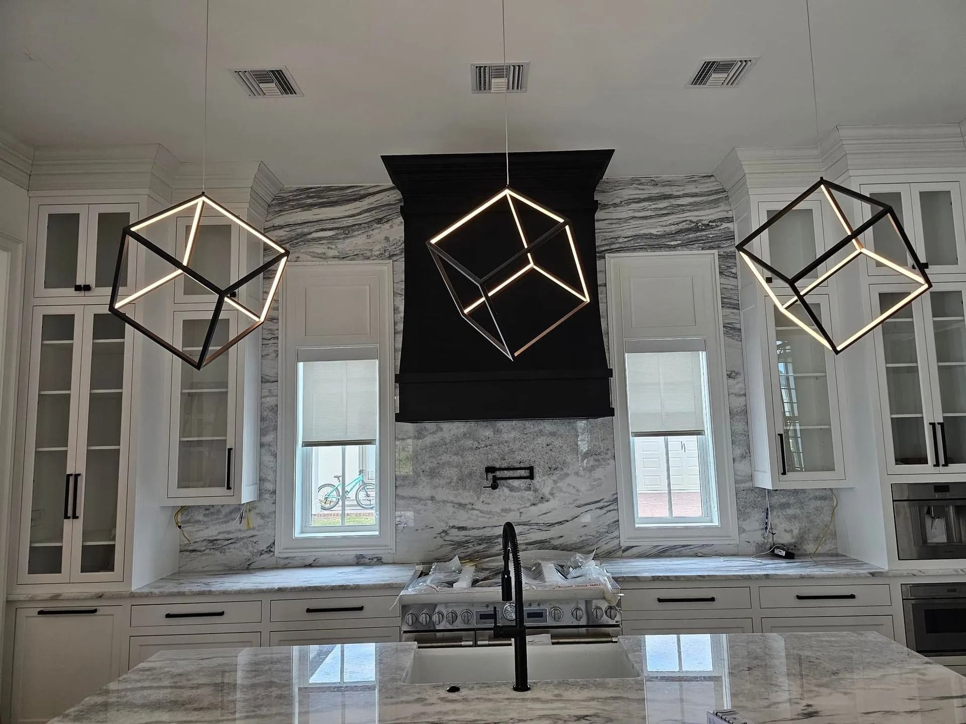 Modern kitchen with marble island, black range hood, and three geometric pendant lights above sink area
