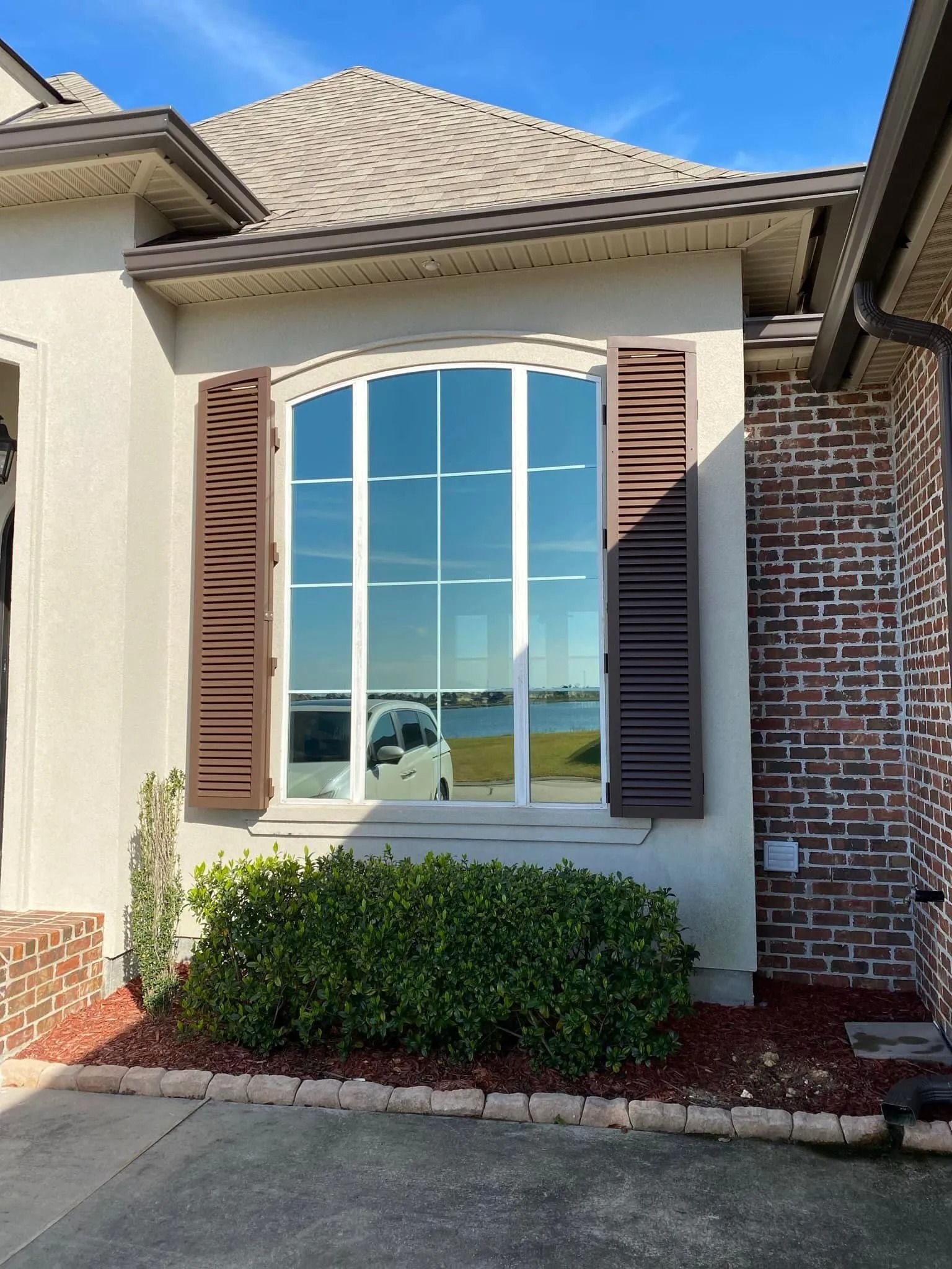 Front exterior of a home with a large arched window, brown shutters, brick siding, and shrubs