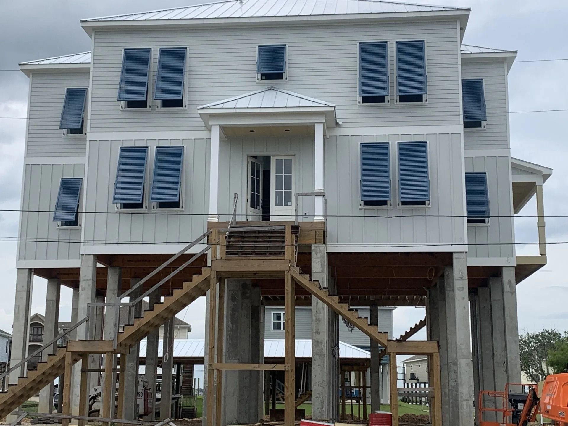 Elevated white house under construction with blue window coverings and exterior stairs on stilts