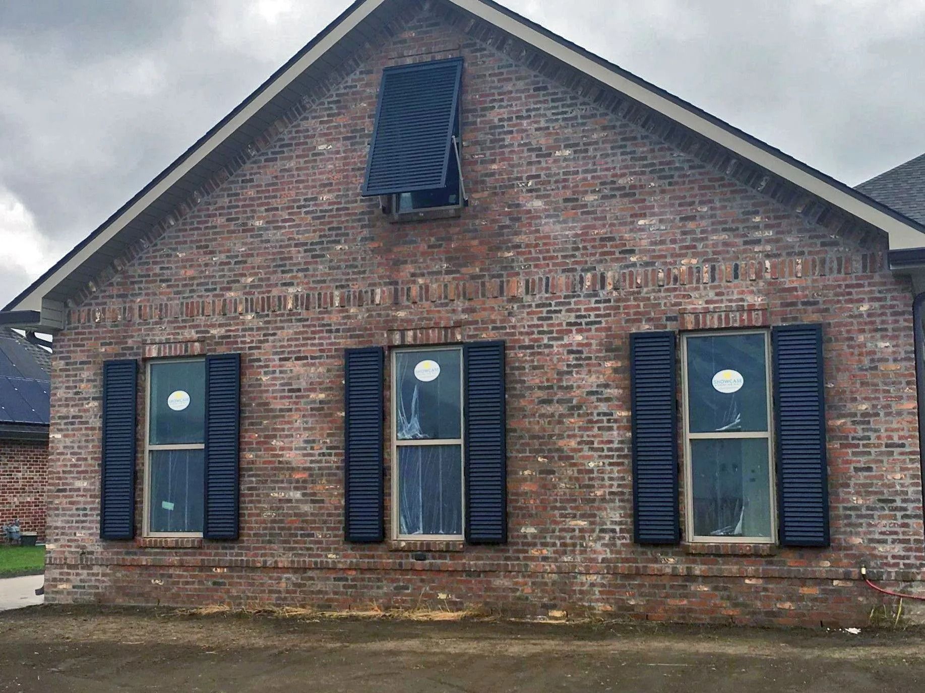Brick building front with three blue-shuttered windows and a central door under a steep roof