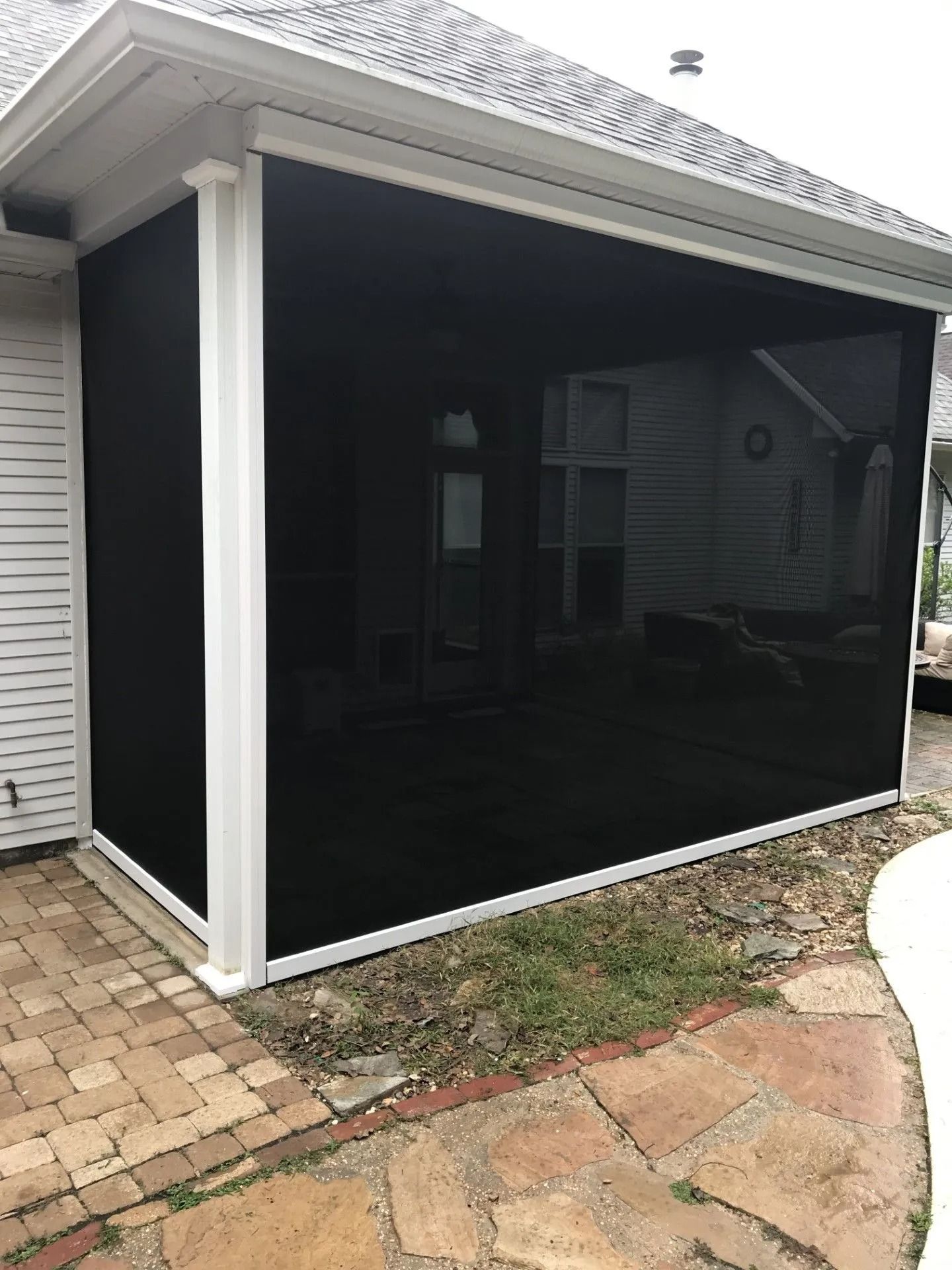 Black screened patio enclosure attached to a white house beside a brick and stone walkway