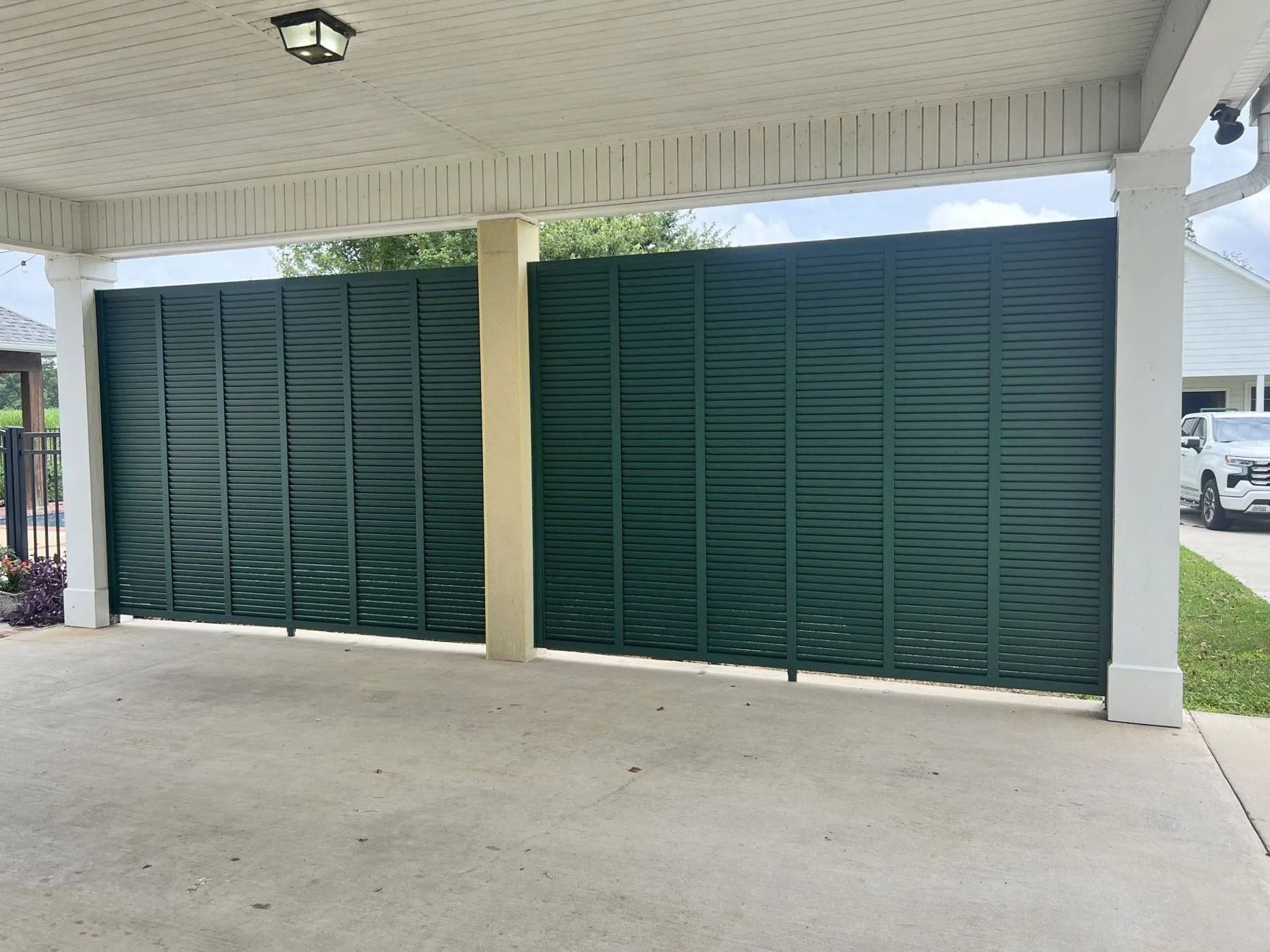Green louvered gates under a covered outdoor area, with white columns and a concrete floor.