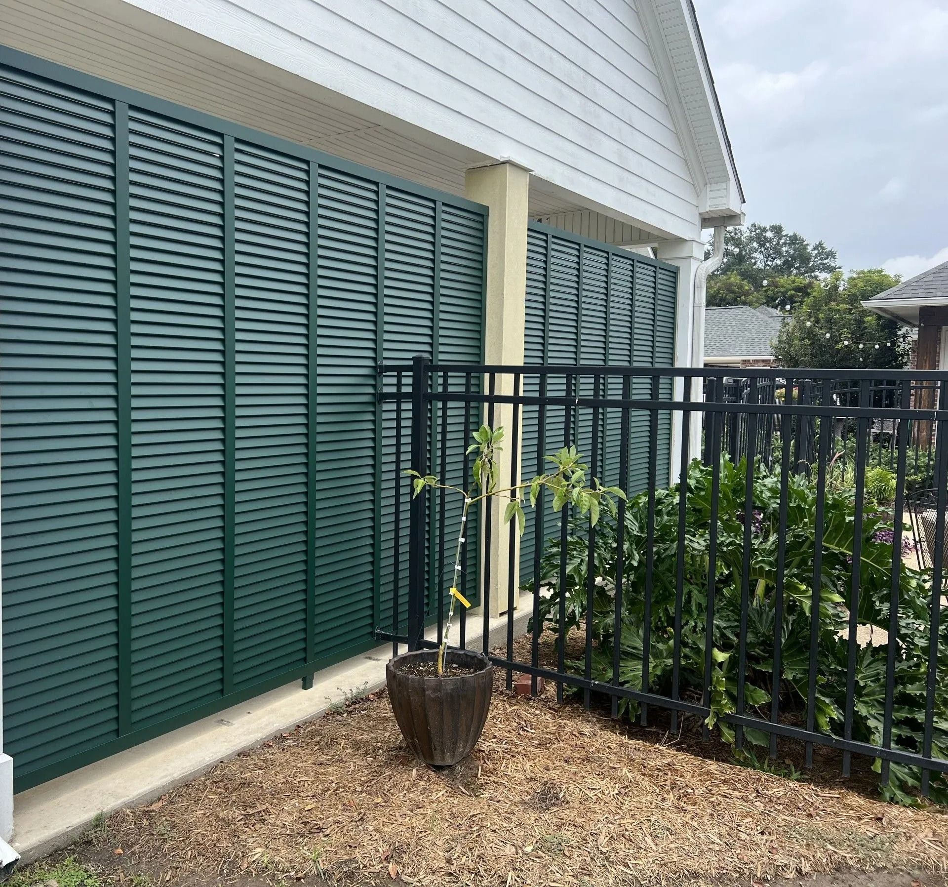 House exterior with green shutters, black fence, and potted plants along a gravel path