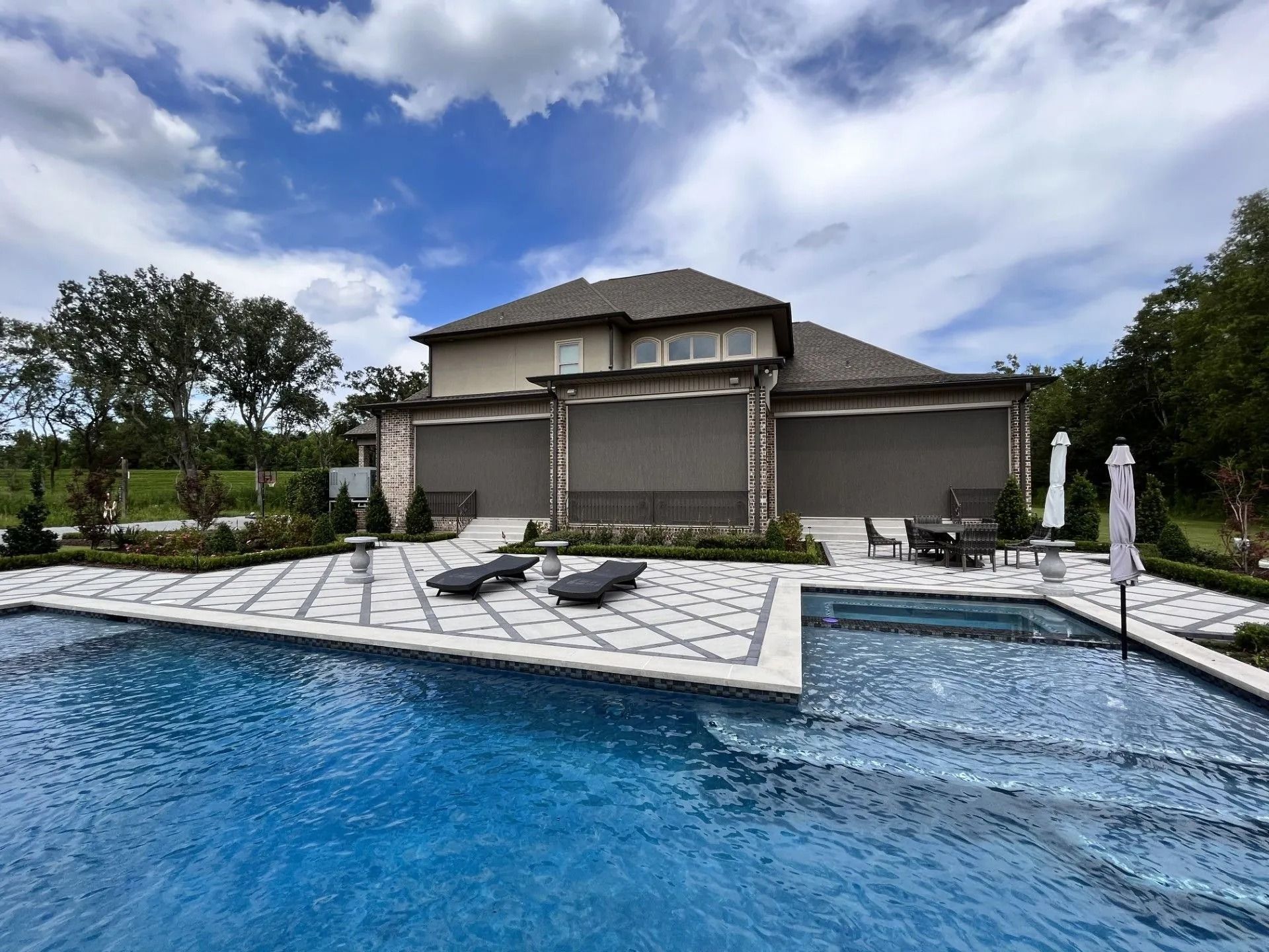 Luxury backyard pool with a modern two-story house under a cloudy sky