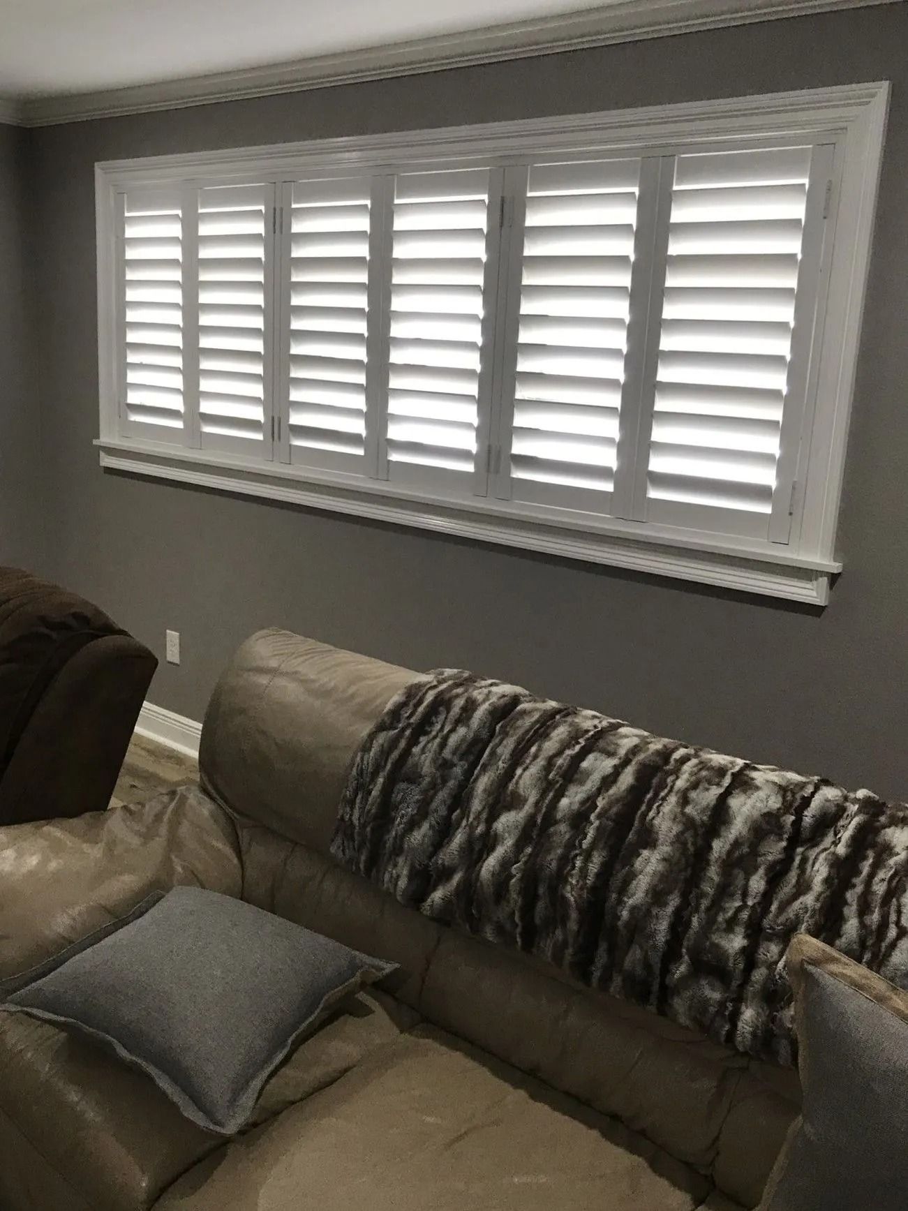 Living room sofa beneath a window with white shutters and gray walls