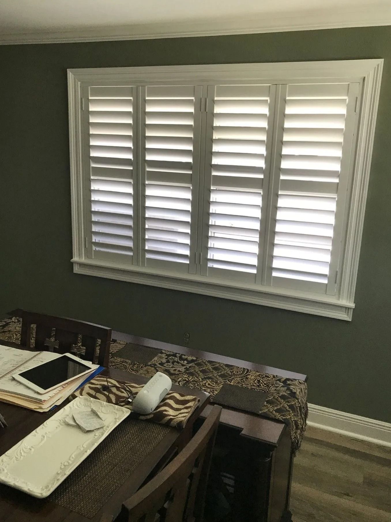 Home office with a desk under a window fitted with white shutters and blinds.