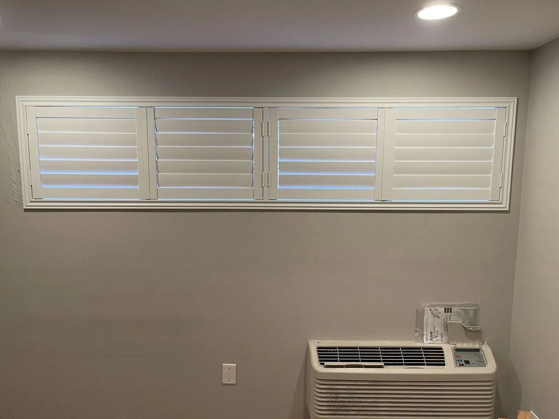 White louvered window above a beige wall with a window AC unit below.