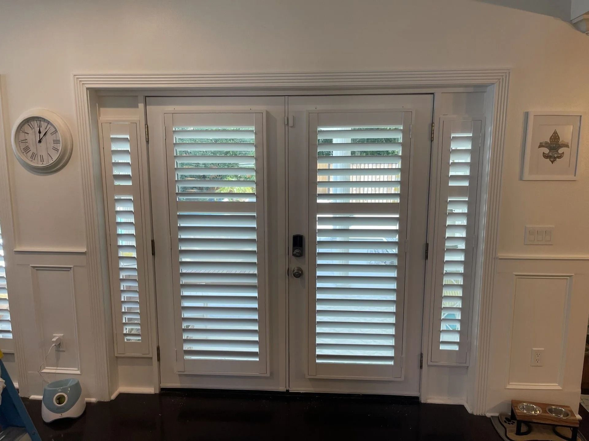 White French doors with shuttered glass panels in a bright room, flanked by wall trim and small decor items.