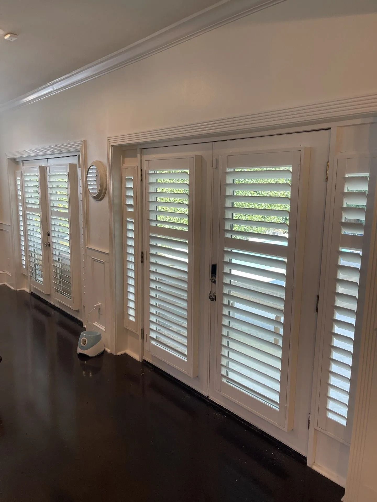 Bright hallway with dark wood floors, white French doors, and plantation shutters letting in daylight