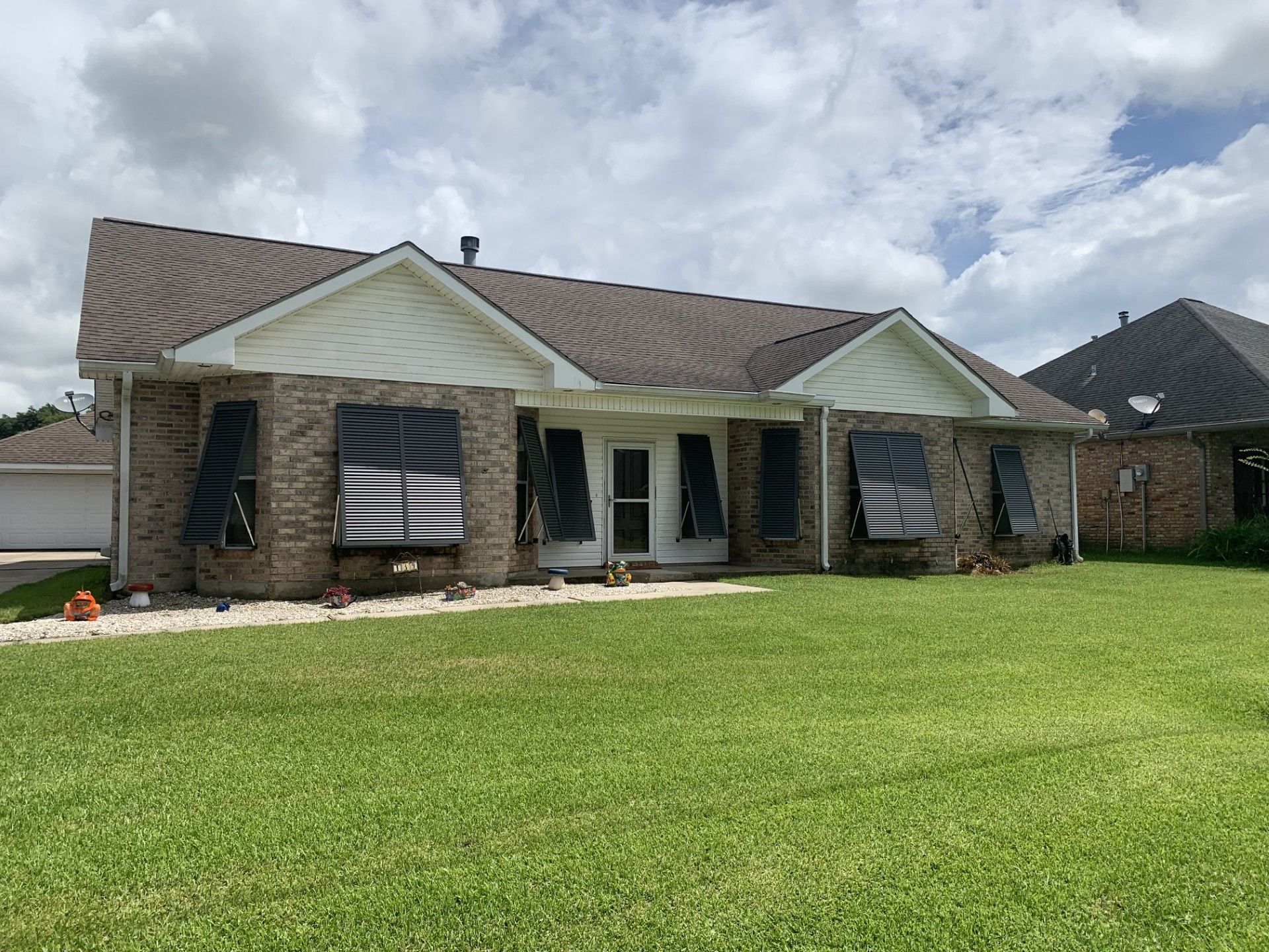 Single-story brick house with a large green lawn and cloudy sky