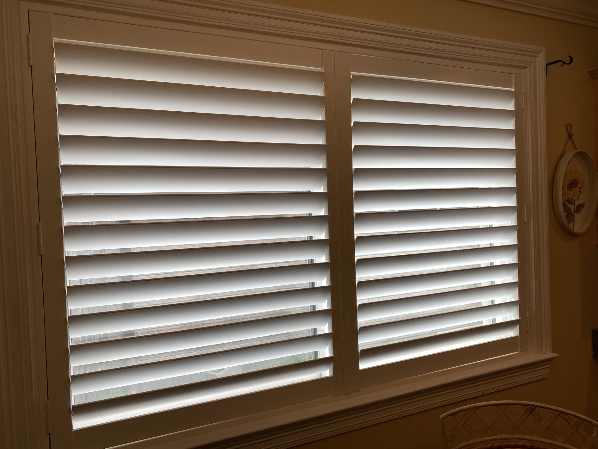 White window shutters on a beige wall with a small hanging decoration and a windowsill below