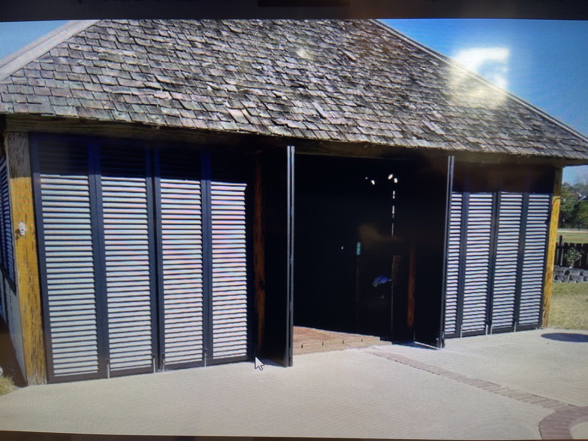 Small rustic wooden building with shuttered windows and a central open doorway in bright sunlight.